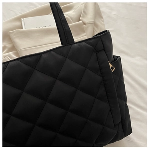 Detail of black quilted tote bag showing padded nylon texture and gold zipper hardware