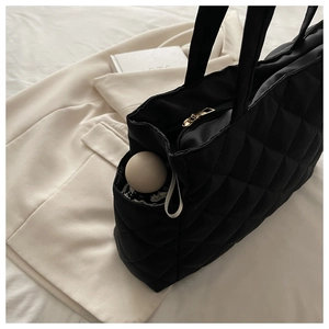 Close-up of black quilted tote bag side pocket with umbrella and golden zipper detail