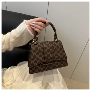 Detail of a brown monogram small square bag with golden hardware held by hand