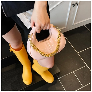 Close-up of pink patent leather handbag with decorative thick gold chain and zipper closure