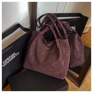 Detail of burgundy suede tote bag featuring distinctive spiral woven handles and gold logo