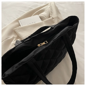 Close-up of black quilted tote bag featuring golden zipper and diamond stitching