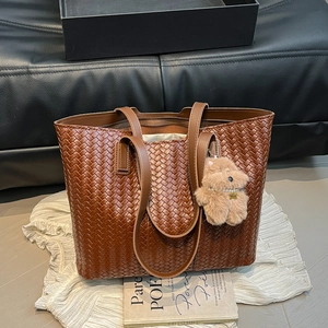 Large dark brown woven tote bag with a cute plush dog charm on a soft fabric background