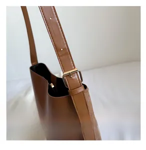 Detail of adjustable golden metal buckle and stitching on a brown leather bucket bag