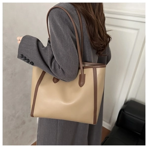 Detail of a large beige tote bag with dark brown trim and reinforced base for daily commute