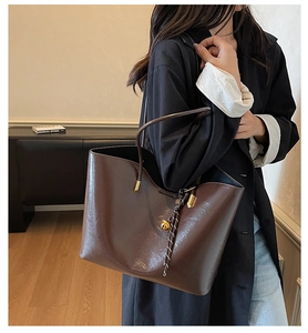 Detail of deep brown glossy tote bag with gold ball charm and long shoulder straps