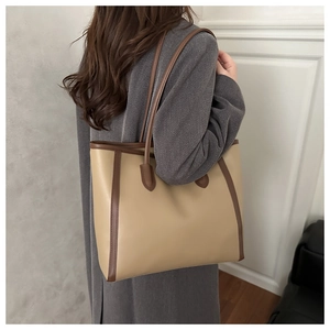 Side view of a large beige tote bag with brown trim on a model wearing a grey wool coat
