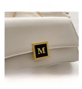 Detail of warm white leather crossbody bag with golden M-logo clasp and chain strap