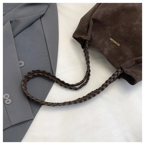 Detail of dark brown suede tote bag featuring braided shoulder straps and gold logo