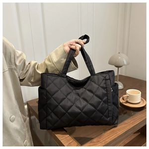 Detail of black quilted tote bag with side pocket and detachable shoulder strap design