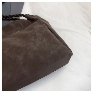 Close-up of deep brown suede tote bag with woven leather handles and logo detail