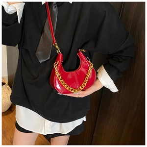 Detailed view of red glossy patent leather dumpling bag with decorative gold chain strap