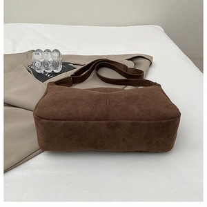 Detail of a brown suede tote bag featuring vertical stitching on a white fabric background