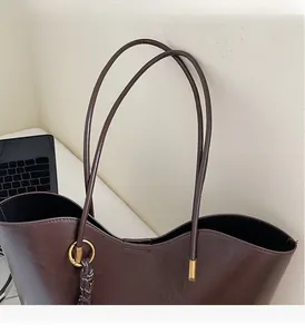 Detail of dark brown tote bag handle with golden rings and woven tassel charm