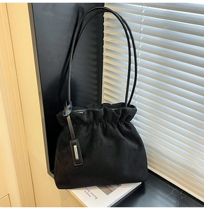 Close-up of black suede bucket bag with pleated design and silver metallic tag detail
