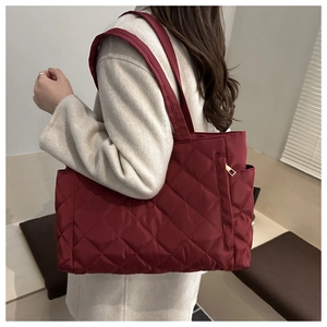 Detail of wine red quilted tote bag with golden metal zipper and glossy nylon texture