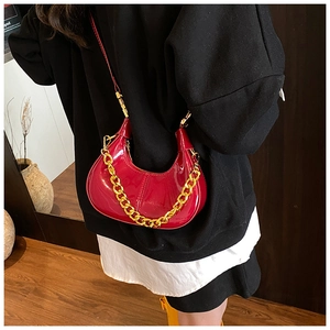 Detail of red patent leather dumpling bag with chunky gold chain on woman back