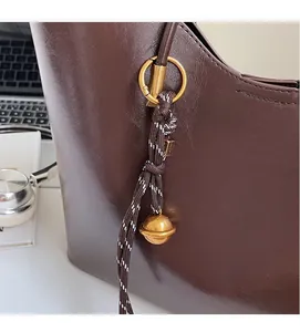 Detailed macro view of woven strap and gold sphere pendant on a brown leather tote bag