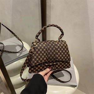 Retro geometric monogram crossbody bag with top handle and gold hardware on stand
