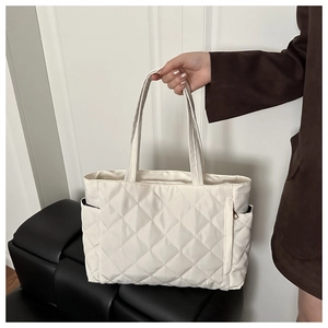 Close-up of beige quilted tote bag showing large diamond stitching and side zipper pocket