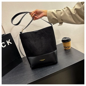 Detail of minimalist black bucket bag featuring suede stitching and golden logo lettering