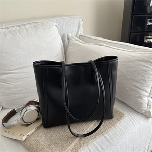 Minimalist black leather tote bag with long straps on a sofa for daily commuting