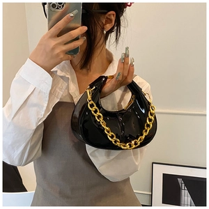 Detail view of black patent leather dumpling bag with chunky gold chain and metal handle