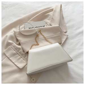 Detail shot of the white trapezoid handbag with gold chain strap on a beige blazer