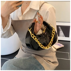 Detail of glossy black patent leather crescent bag with chunky gold chain hardware