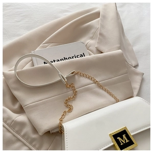 Close-up of white leather crossbody bag with golden M buckle on beige blazer jacket