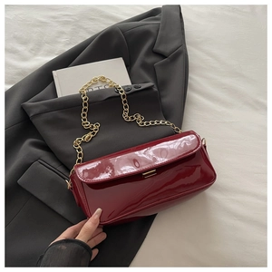 Détail du sac à main en cuir verni bordeaux avec chaîne dorée sur blazer gris