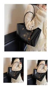 Detail of black glossy tote bag featuring golden artistic print and woven bell charm