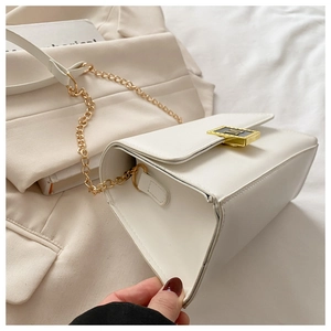 Detail of white leather crossbody bag with gold chain strap and M-shaped metal buckle
