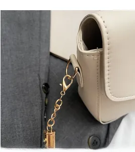 Detail of cream leather square bag showing golden metal lobster clasp and clean stitching