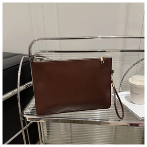 Deep brown envelope clutch with golden zipper and wrist strap on minimalist shelf