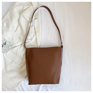 Top view of minimalist brown leather bucket bag on white fabric with gold hardware detail