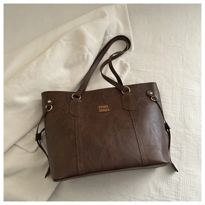Detail of vintage brown leather tote bag showing golden metallic logo and handle rings