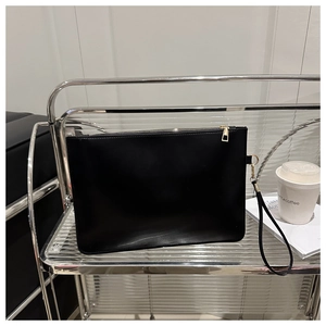 Close-up of minimalist black leather clutch bag with golden zipper on metal rack
