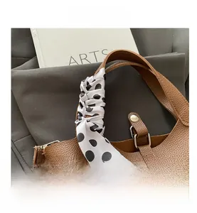 Detailed macro view of brown lychee grain leather handbag with polka dot silk scarf handle