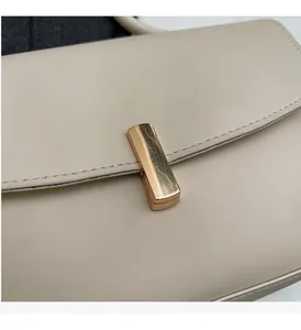 Close-up of a polished golden rectangular metal buckle on a cream leather shoulder bag