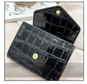 Detail of black crocodile patent leather clutch with a round gold snap button closure