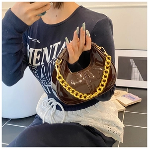 Detailed view of dark brown patent leather dumpling bag with thick gold chain strap