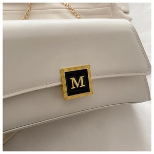 Detail of cream leather crossbody bag featuring a golden M logo buckle and chain strap