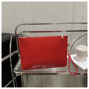 Macro detail of red leather clutch bag with golden zipper and wrist strap on a glass shelf