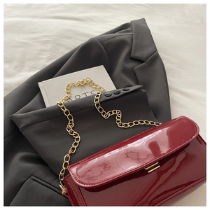 Détail du sac à main en cuir verni rouge avec chaîne dorée sur veste de blazer grise