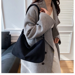 Minimalist black tote bag shown on a model side-shoulder view in a modern indoor setting