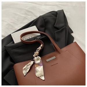 Detail of a brown leather tote bag with printed silk scarf and metallic bar ornament
