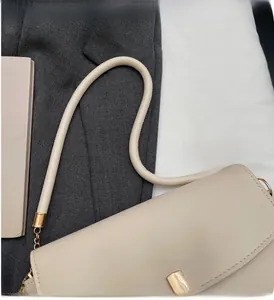 Close-up of beige faux leather handbag with cylindrical handle and gold metal chain hardware