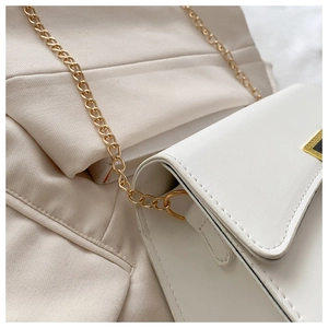 Detail of white faux leather crossbody bag with gold chain strap and square metal buckle