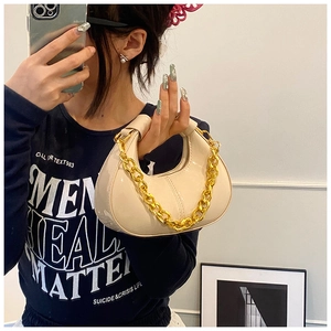Detail of a creamy hobo bag with a shiny finish and bold gold chain shoulder strap